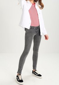 Jeans ajustados grises con un corte de altura media, combinados con una camiseta de rayas rojas y blancas y una chaqueta de mezclilla blanca. Zapatillas en blanco y negro.