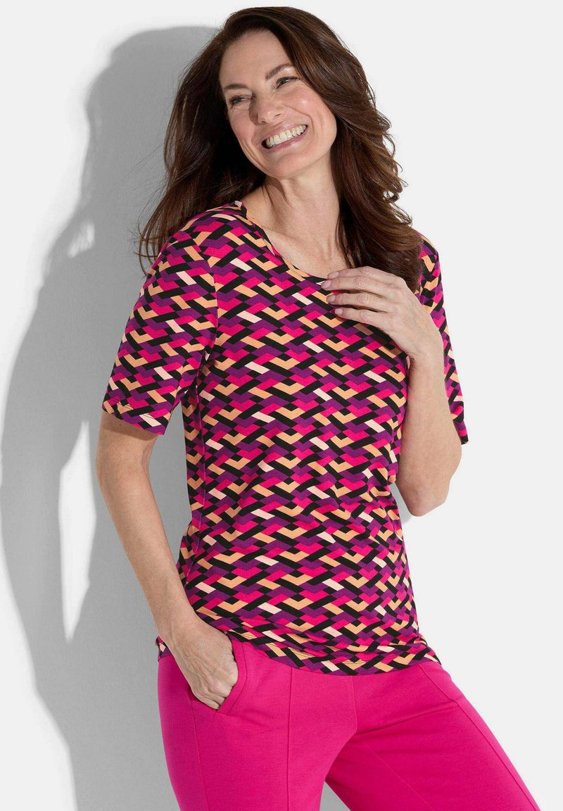 Multikleurige top met een geweven patroon in roze, zwart en tan, gecombineerd met felroze broek. Korte mouwen en een ronde halslijn.