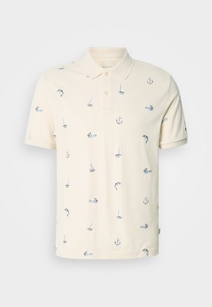 Polo crème à manches courtes avec col et boutons, ornée de petits motifs nautiques bleu marine représentant des voiliers, des ancres et des dauphins.
