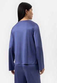 Langarmtop van diepblauwe stof met een gladde textuur. Heeft een brede, ronde halslijn en een ontspannen pasvorm, in combinatie met bijpassende broek.