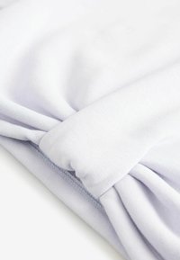 Tissu en coton bleu clair avec une texture lisse, présentant un détail tordu à une extrémité et des bords cousus.