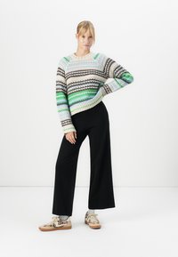 Gestreepte trui in beige, zwart, groen en blauw, gecombineerd met zwarte wijde broek en beige sneakers met een luipaardpatroon.