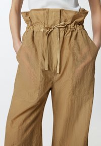 Bež hlače širokih nogavica od teksturirane tkanine s elastičnim pojasom ivezicom, s dva prednja džepa i slobodnim krojem.