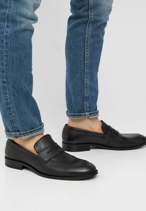 Zwarte leren loafers met een gladde afwerking, voorzien van een verhoogde banddetail op de bovenkant, gedragen met opgerolde blauwe jeans.