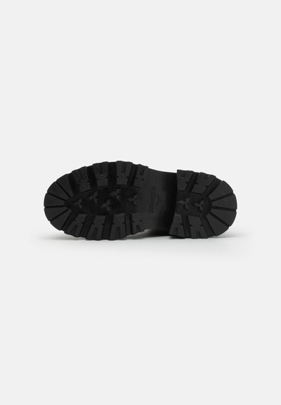 Suela de zapato de goma negra con una textura profunda y una superficie texturizada, que presenta patrones de tracción prominentes para mejorar el agarre y la estabilidad.