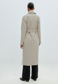 Lange beige jas, fitted design met een riem in de taille, gebreide stof, geknoopte kraag, rechte silhoët en zijnaad.
