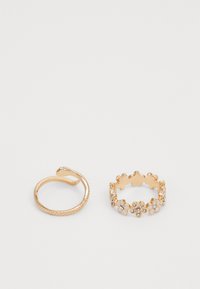 Due anelli d'oro: un anello aperto a forma di serpente curvato e un anello con design floreale decorato con piccole pietre e fiori bianchi.