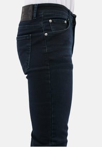 Donkerblauwe spijkerbroek met een getailleerde pasvorm, met een leren label op de taille en zilveren hardware details op de zakken.