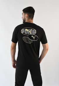 Camiseta de algodón negra con un gran gráfico que incluye el texto "PUMA" y dos logotipos en dorado y blanco en la parte de atrás. Mangas cortas, corte regular.