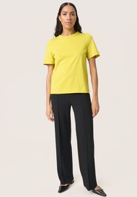 Yellow short-sleeve t-shirt paired with black fitted trousers. T-shirt has a round neckline; trousers are tailored with a straight cut and clean lines.