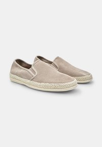 Beige slip-on cipők perforált velúrból, fonott jute talppal, lekerekített orral és rugalmas oldalsó panelekből az egyszerű felhúzás érdekében.