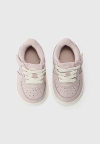 Sneakers Nike in pelle rosa chiaro, punta rotonda, suola bianca testurizzata, dettagli perforati e lacci avorio con cinturino in Velcro per una vestibilità sicura.