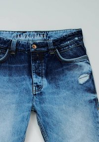 Vaqueros de mezclilla en azul medio con un lavado descolorido, que cuentan con un desgastado rasgado en el bolsillo derecho, botón de latón y diseño de cinco bolsillos.
