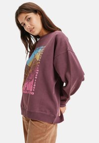 Bordeaux sweatshirt met een grafische print van bergen en golven, voorzien van een ronde hals en geribde manchetten, gecombineerd met corduroy broek.