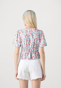 Top con stampa floreale, maniche corte a palloncino, vita arricciata e sfondo azzurro chiaro. Abbinato a pantaloni corti bianchi strappati.