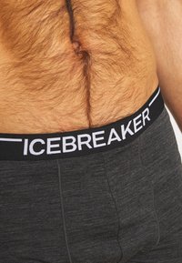 Fekete Icebreaker boxer alsónadrág fehér logóval a derékrészen, textúrált, sötétszürke anyagból készült. Zsugorított kép a derékrészről és a test részéről.