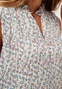 Blusa floral plisada en tejido ligero. Presenta un escote suave con volantes y un patrón pastel en tonos de rosa, azul y verde.