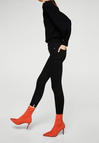 Jeans ajustados negros combinados con un suéter negro de gran tamaño y vibrantes botines naranjas que presentan una punta afilada y tacón de aguja.