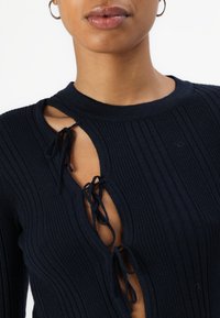 Top de punto acanalado en navy con un diseño de corte y lazos ajustables en la apertura, que presenta un cuello redondo y una textura en la tela.
