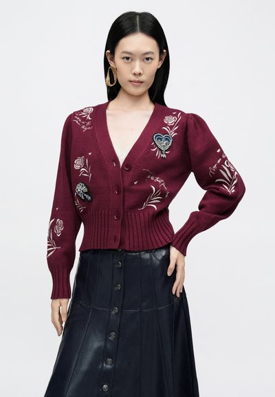 Bordowy dzianinowy kardigan z kwiatową haftem, bufkami na rękawach, dekoltem w serek i prążkowanym dołem. Połączony z ciemną skórzaną spódnicą i wyrazistymi kolczykami.