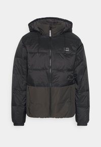 Black and dark green puffer jacket with a hood, zippered front, and elastic cuffs. Features a logo patch on the chest and a paneled design.