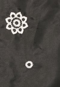 Tessuto nero con ricami floreali bianchi, caratterizzato da un grande disegno di fiore e un motivo circolare più piccolo. Texture liscia e cuciture dettagliate.
