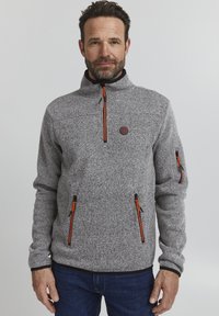 Pulover gri din fleece cu guler înalt, având șnururi de fermoar negre și portocalii și două buzunare frontale cu fermoar. Material texturat cu detaliu logo.