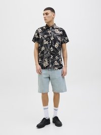 Chemise boutonnée noire à manches courtes avec un motif floral blanc, associée à un short en jean bleu clair, des chaussettes blanches et des chaussures noires.