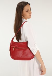 Rote Leder-Schultertasche mit strukturiertem Finish, vorderer Reißverschlusstasche und einem einstellbaren Tragegurt. Das Design ist schlank und praktisch.