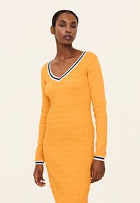 Langärmliges, enganliegendes Kleid in leuchtendem Gelb mit strukturiertem Stoff. Verfügt über einen tiefen V-Ausschnitt und kontrastierende marineblaue und weiße Streifenakzente.