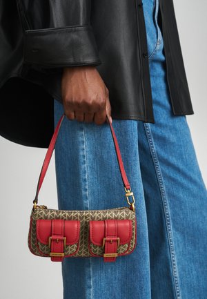 Borsa a tracolla rossa e beige con doppie fibbie, motivo a monogramma, materiale in pelle e manico corto, tenuta da una persona in denim.