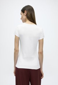 Λευκό κοντομάνικο μπλουζάκι με στρογγυλή  λαιμόκοψη, λείο ύφασμα και εφαρμοστή σιλουέτα, συνδυασμένο με σκούρο βυσσινί παντελόνι.