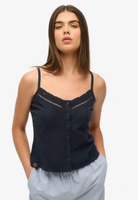 Mørkeblå camisole med blondekant, teksturerede lodrette striber og knapper foran. Letvægtsstof, tynde stropper og en afslappet pasform. Stribede bukser.