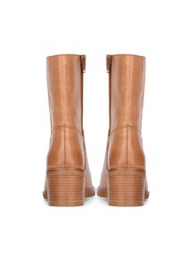 Botas de tobillo de cuero marrón claro con un acabado brillante, cremalleras laterales y tacones apilados. Detalle de costura notable a lo largo de la costura trasera.
