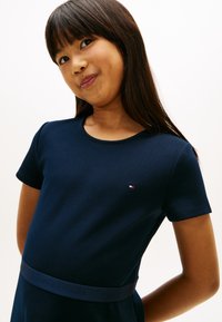 Σκούρο μπλε φόρεμα με κοντά μανίκια και στρογγυλή λαιμόκοψη, με ζώνη λογότυπου σε όμοια απόχρωση γύρω από τη μέση και μικρό λογότυπο στο στήθος.