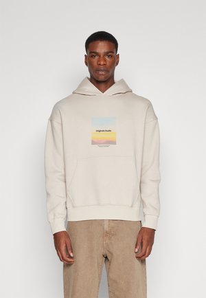 Lichtbeige hoodie met een voorzak en een trekkoordkap. Heeft een rechthoekige graphic in pastelkleuren, gelabeld "Originals Studio."