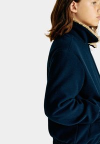 Granatowa polarowa kurtka z wysokim kołnierzem, beżowym wykończeniem i bocznymi kieszeniami. Charakteryzuje się luźnym krojem oraz ściągaczami na mankietach i dolnej krawędzi.