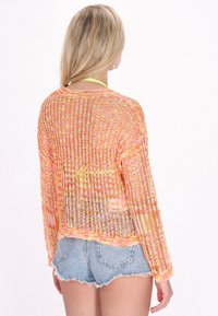 Maglione a maglia con trama aperta in tonalità di arancione e giallo, con maniche lunghe e vestibilità rilassata, abbinato a pantaloni corti in denim. Testurizzato e leggero.