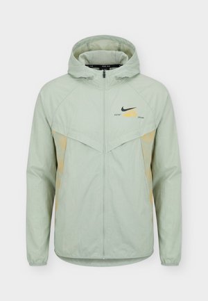 Hele-roheline Nike kapuutsiga jakk, millel on täis tõmblukk, elastsed mansetid ja "Distant Dreams" tekst musta Nike logoga rinnal.