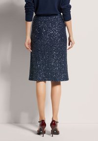 Marineblauw pailletten kokerrok met een gestructureerde oppervlakte, knie-laag, gecombineerd met bordeauxrode hoge hakken. Glad gevoerd interieur.