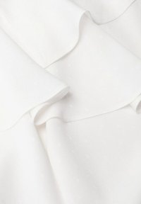 Tissu blanc avec des volants superposés, montrant une texture douce et des détails de couture subtils.