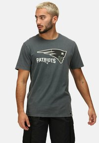 Šedé bavlněné tričko s logem "Patriots" v bílé a černé barvě, s kulatým výstřihem a krátkými rukávy. Volný střih, minimální textura.