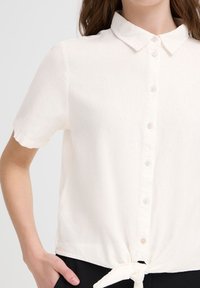 Camicia bianca a maniche corte realizzata in tessuto leggero, con colletto, chiusura a bottoni e dettaglio con orlo annodato.
