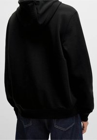 Sweat-shirt à capuche noir avec une coupe décontractée, fabriqué en tissu texturé, avec des poignets et un ourlet côtelés, et un design simple. Détails de couture visibles.