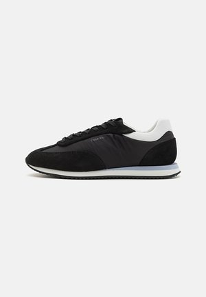 Sneaker nera con upper in suede e tessuto, tallone bianco, punta rotonda, lacci neri e suola testurizzata a contrasto. Logo del marchio sul lato.