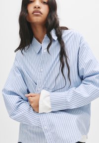 Blå og hvid stribet button-up skjorte, løs pasform, med krave, lange ærmer og kontrast detaljer i hvid ved manchetterne. Elegant bomuldsstof.