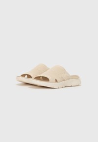 Beige glidende sandaler med mesh-overdel som har utskjæringer, myk såle og teksturert design. Lettvekts og uformell fottøyvalg.