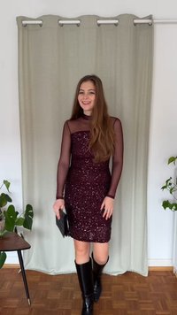 Vínové šaty bez rukávů se zdobením z flitrů a průsvitnými dlouhými rukávy; doplněné černými kozačkami po kolena a černou psaníčkovou kabelkou.