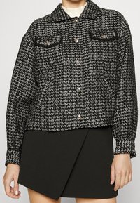 Svart och vit tweedjacka med två bröstfickor, silverfärgade knappar och krage. Strukturväv med fyrkantig form och långa ärmar.