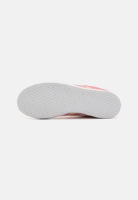 Rosa sneakers med en texturerad vit gummisula som visar intrikata mönster. Ovandelen har mjukt textilmaterial med kontrasterande rosa accenter.